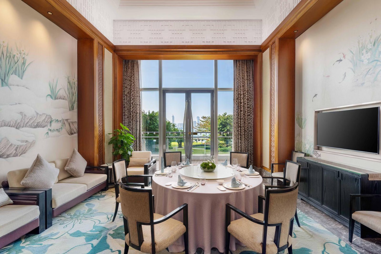 中式包廂裡的大圓桌擺好餐具，牆上是水墨花草壁畫，挑高落地窗外是草坪、樹木與遠處高樓