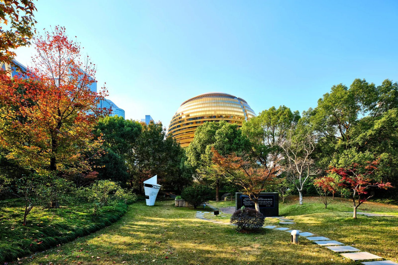 從秋天的公園草地與紅葉樹林望向杭州國際會議中心洲際酒店的金球造型大樓