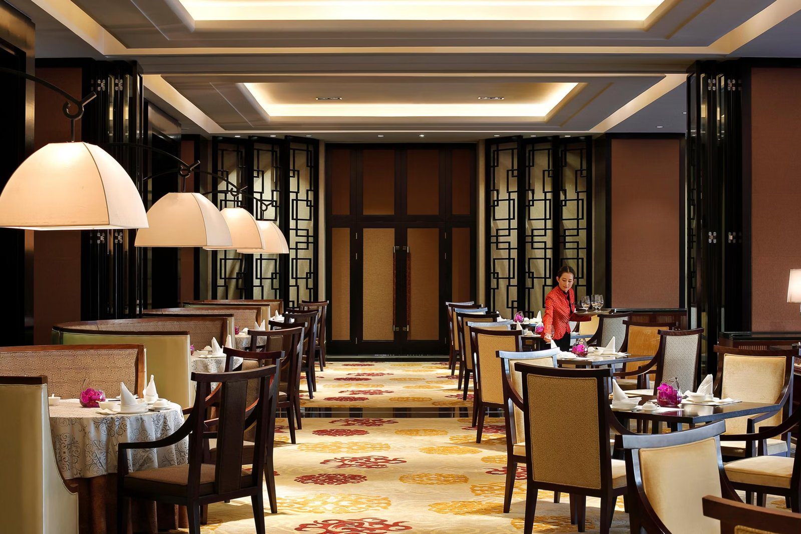 昆明洲際酒店香稻軒中餐廳用餐區，黑色鏤空屏風與大燈罩吊燈下擺著餐桌，地毯是紅黃花紋