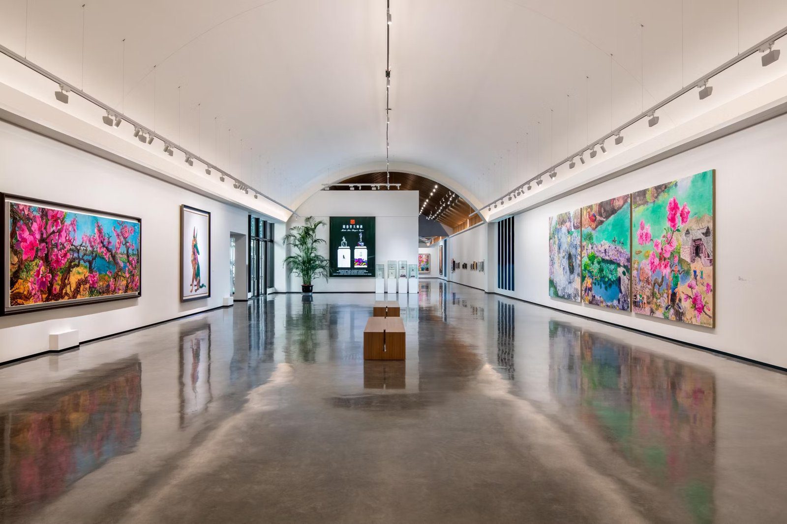 拱頂展廳內，兩側白牆掛著大幅桃花油畫與兔子畫作，地面是光亮的水泥地，中央擺著木長凳