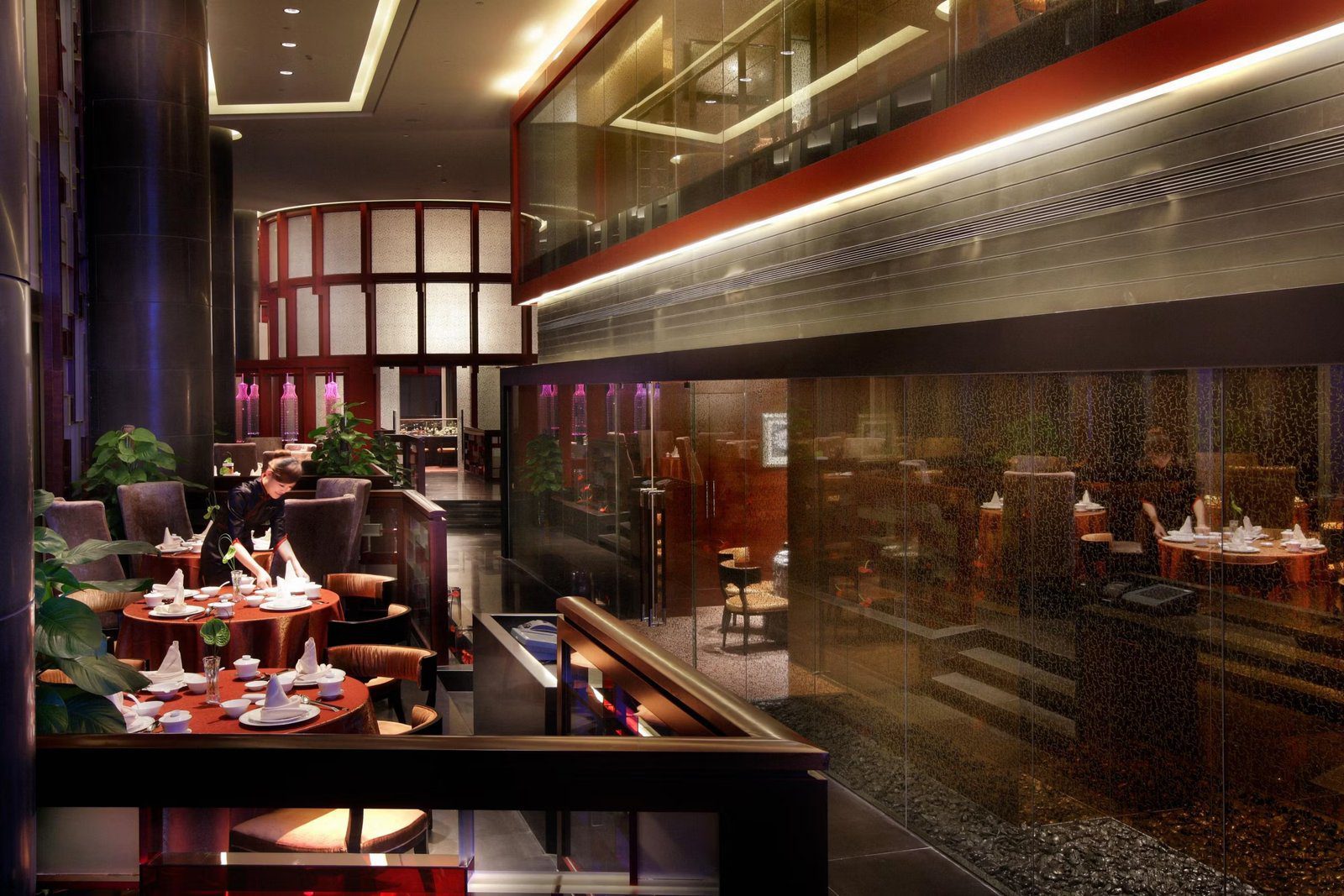 南京綠地洲際酒店凌霄中餐廳，服務員在鋪紅桌布的圓桌前擺設餐具，右側是玻璃隔間的用餐區