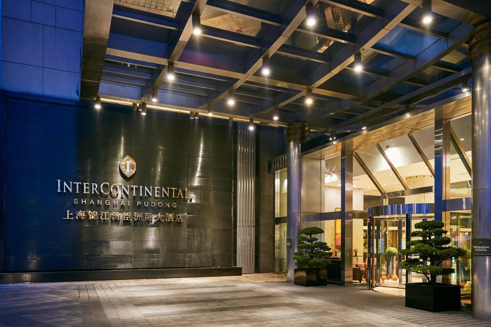 上海錦江湯臣洲際大酒店夜間入口,雨遮下的黑色牆面掛著 INTERCONTINENTAL SHANGHAI PUDONG 招牌,右側是旋轉門與兩盆造型松
