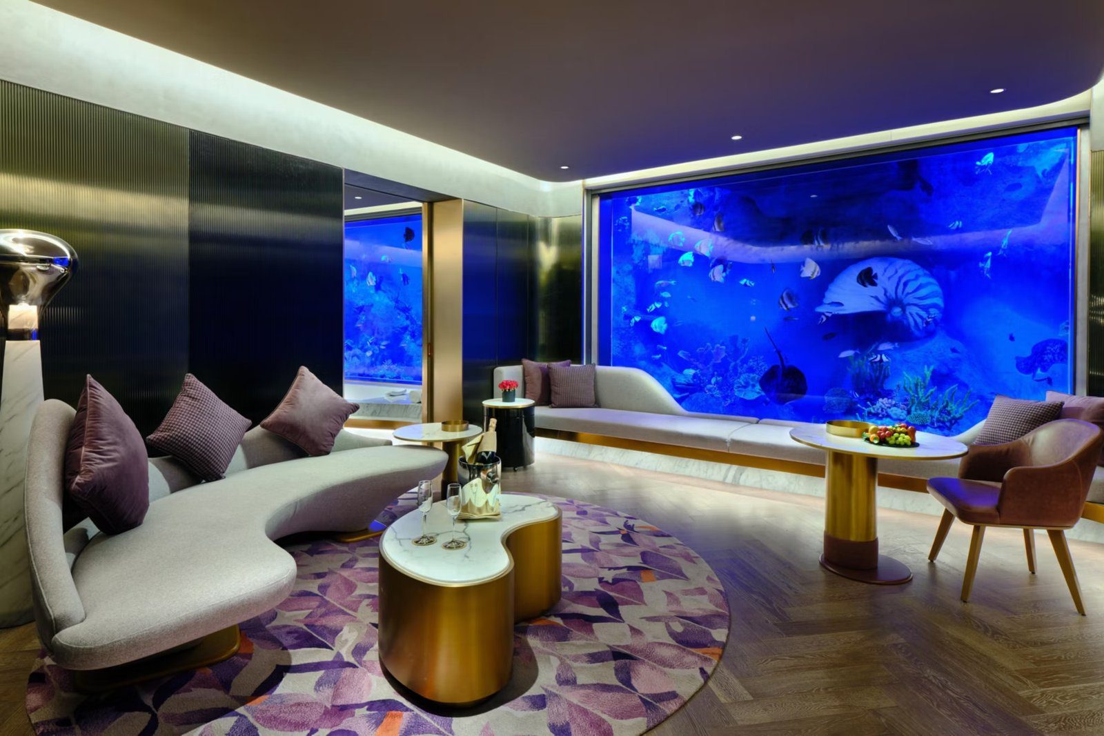 上海佘山世茂洲際酒店水下景觀套房的起居區,右側整面水族展示牆裡有珊瑚與熱帶魚,前方是弧形淺灰沙發與金色茶几