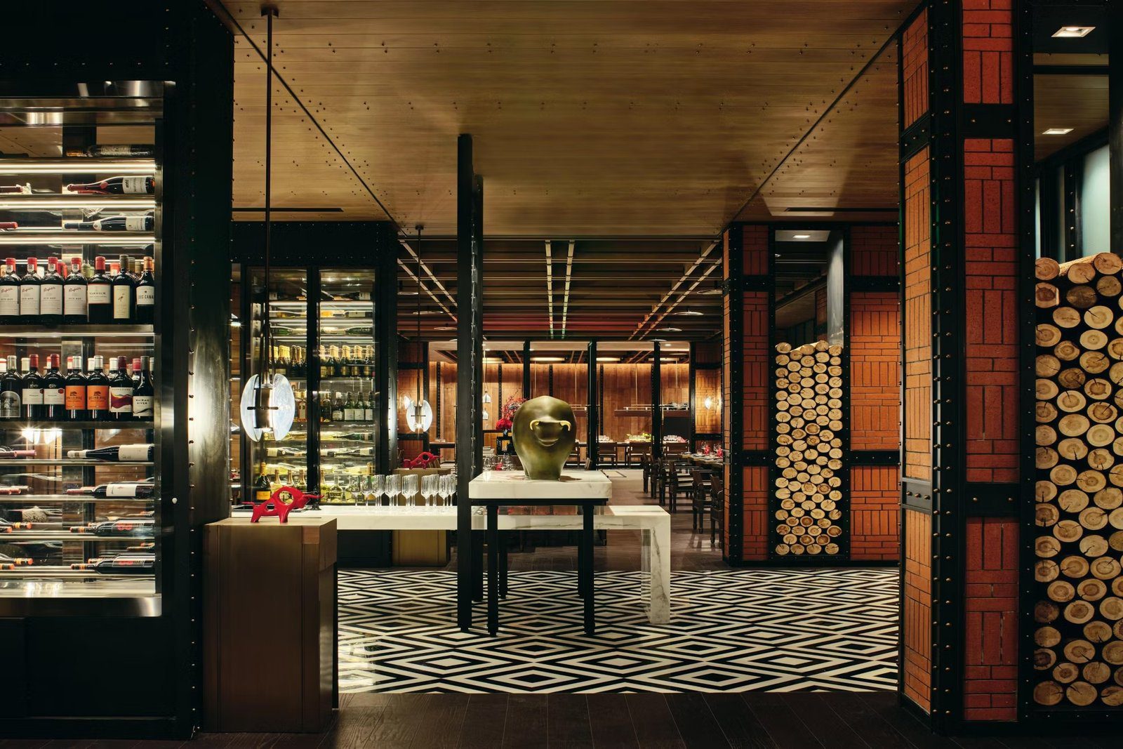 西安經開洲際酒店恰 CHAR 餐廳的入口，左側是整面玻璃酒櫃，中央白色石檯上擺著金色牛頭雕塑，右側紅磚柱旁堆著木柴，地面是黑白菱形花磚