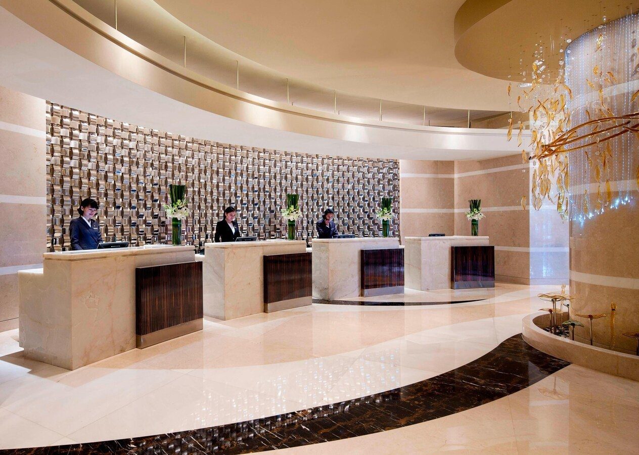 杭州 JW 萬豪酒店大堂的弧形接待櫃檯、金屬馬賽克背牆與三名櫃檯人員