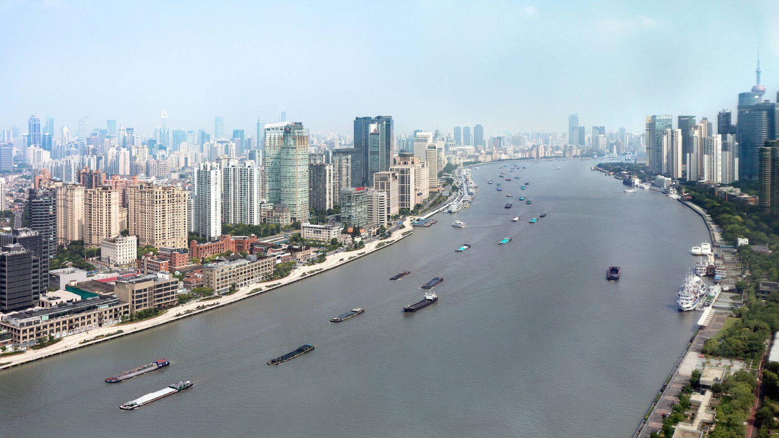從高樓俯瞰黃浦江,江面有多艘貨船通行,兩岸是上海市區街廓與高樓天際線