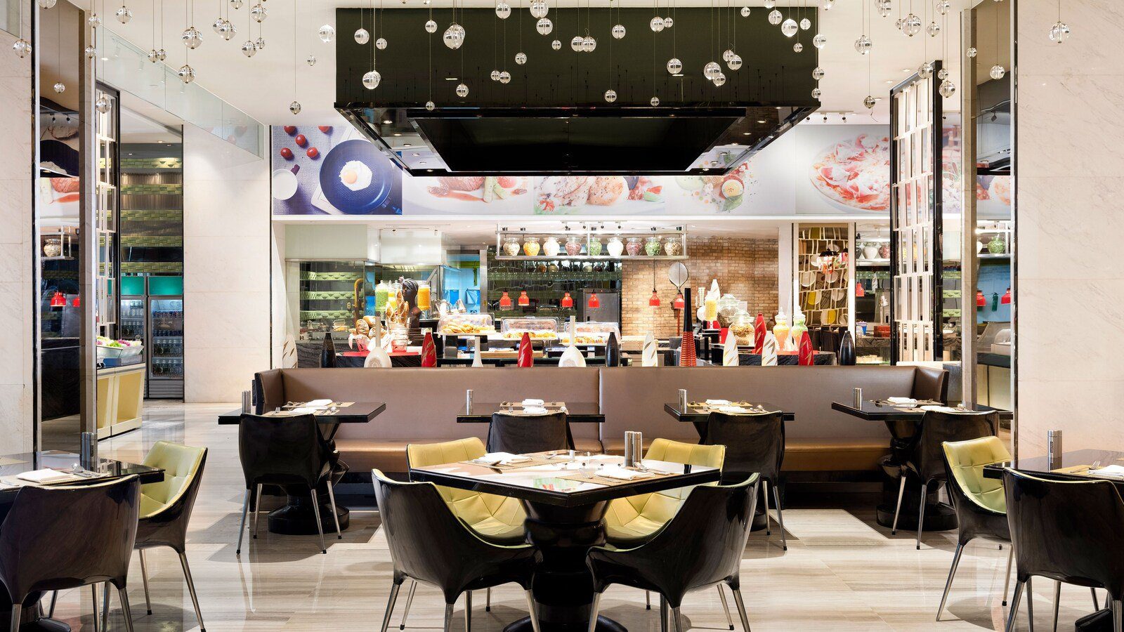 青島富力艾美酒店新食譜自助餐廳，黑色餐桌配黃綠色椅子，後方是自助餐檯與料理照片裝飾牆
