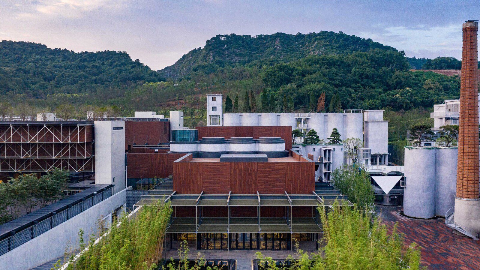 南京珺懋酒店日間的鳥瞰,紅磚廠房、灰色筒倉與高聳的磚造煙囪背靠山丘