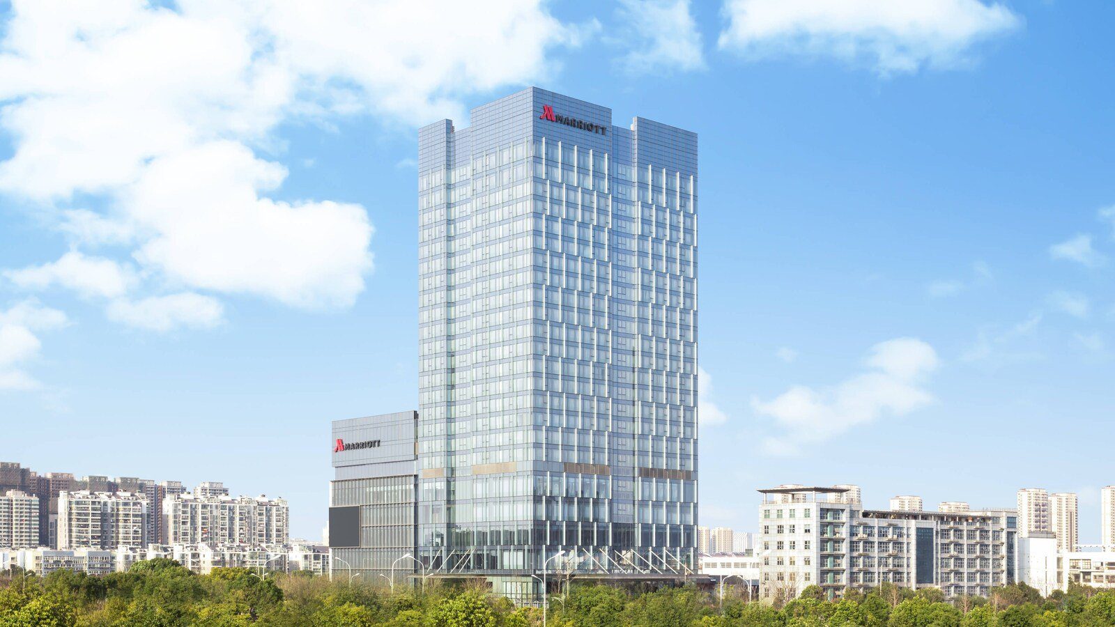 藍天白雲下的南京景楓萬豪酒店玻璃塔樓，頂端有紅色 MARRIOTT 招牌