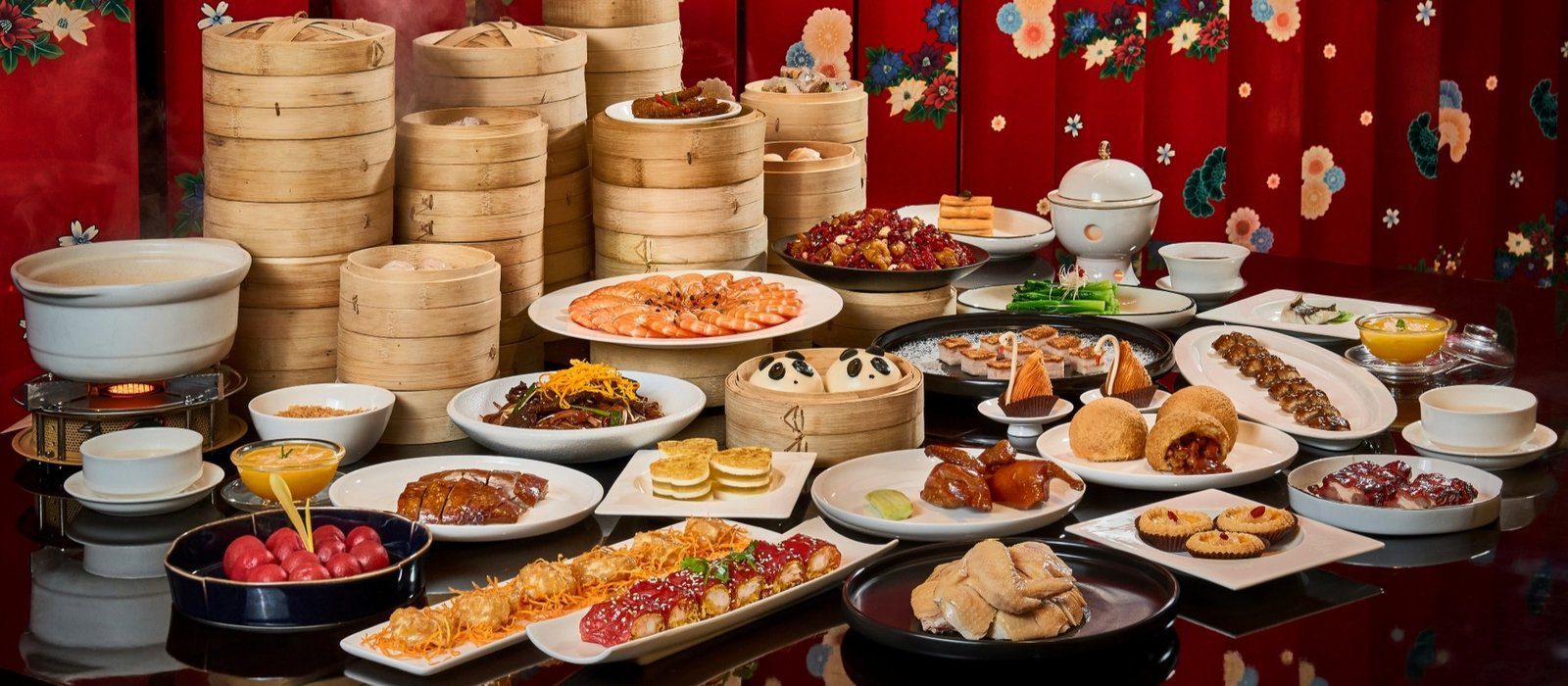玥軒的粵式點心與菜色擺滿深色圓桌，後方疊著多層竹蒸籠，盤中有白灼蝦、燒鴨、脆皮捲與兩個捏成熊貓臉的白饅頭，背景是印著花卉圖案的紅色屏風