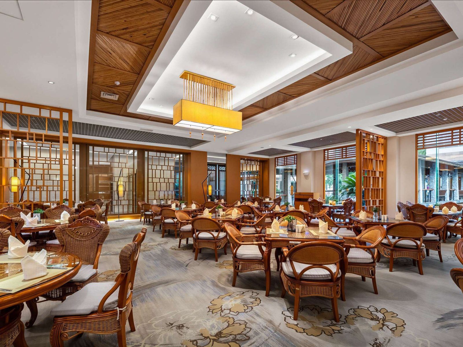 張家界京武雅高鉑爾曼酒店館內的餐廳，一排排藤編扶手椅圍著木桌，天花板是斜紋木條與金色方形吊燈，兩側立著木格屏風