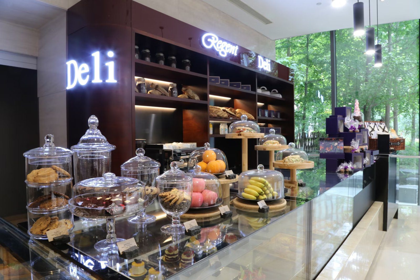 北京麗晶酒店 Deli 櫃台的餅乾罐、三明治與窗外綠樹