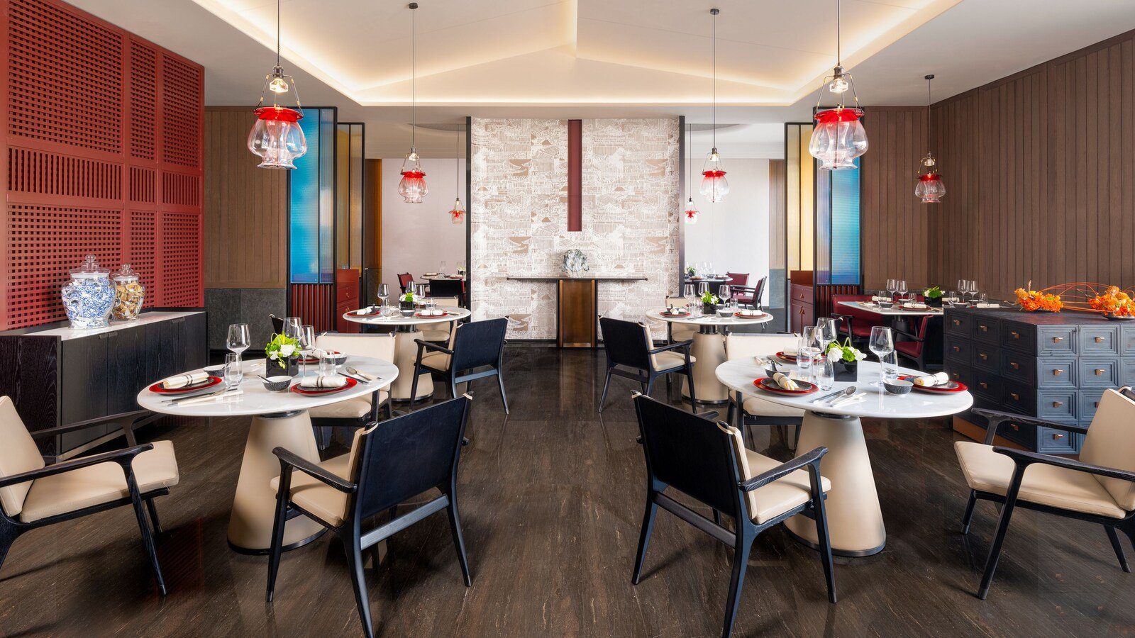 青島金茂萬麗酒店韶舞中餐廳，白色圓桌配深色椅子，上方垂吊紅色玻璃燈