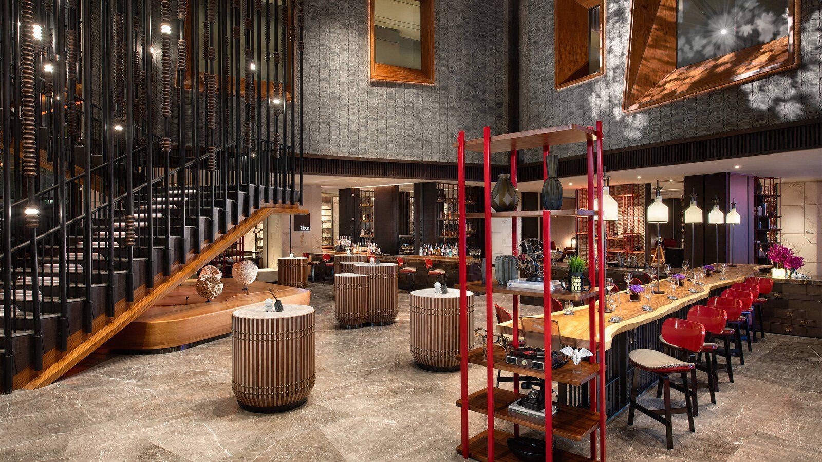 西安萬麗酒店的 R Bar，挑高空間左側是黑色格柵樓梯，右側是原木長吧檯與一排紅色高腳椅，紅色鐵架上擺著器物，後方是酒櫃