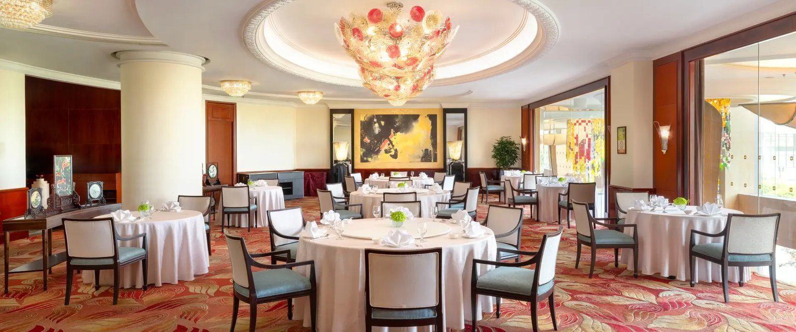 香宮中餐廳的用餐區，多張鋪白桌布的圓桌配深色木框扶手椅，天花懸著紅白相間的大型花球吊燈，地毯是紅金色曲線圖紋
