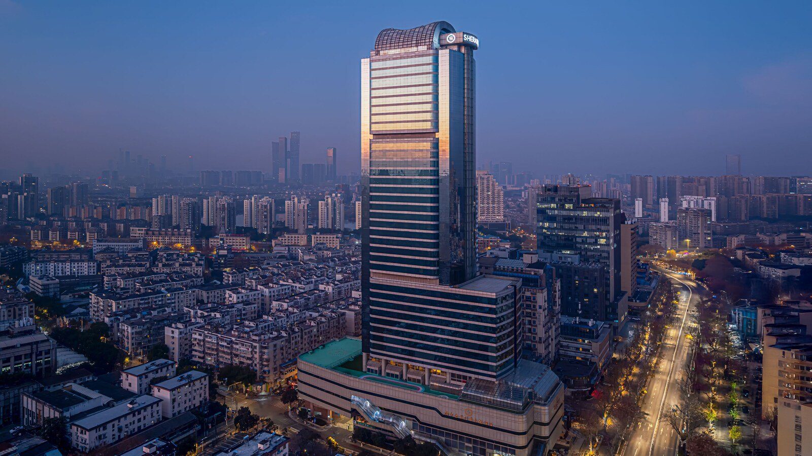 傍晚的南京金絲利喜來登酒店塔樓,頂端有 SHERATON 招牌,右側是亮著路燈的漢中路