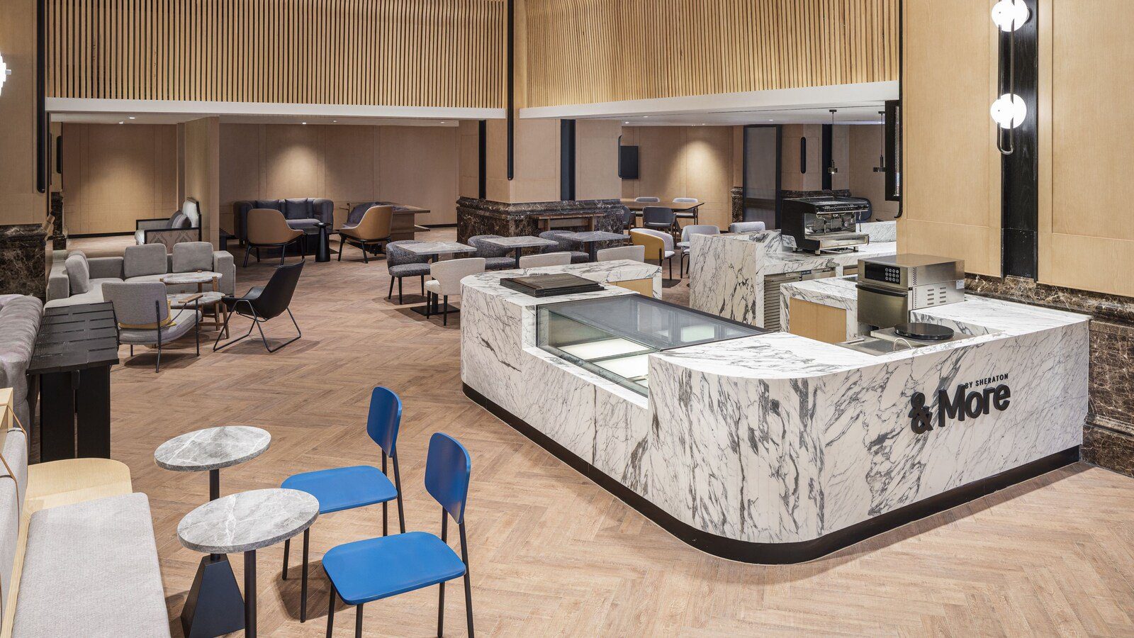 南京金絲利喜來登酒店的 &More by Sheraton 咖啡吧，大理石吧台上有咖啡機，周圍擺著藍色椅子與沙發座