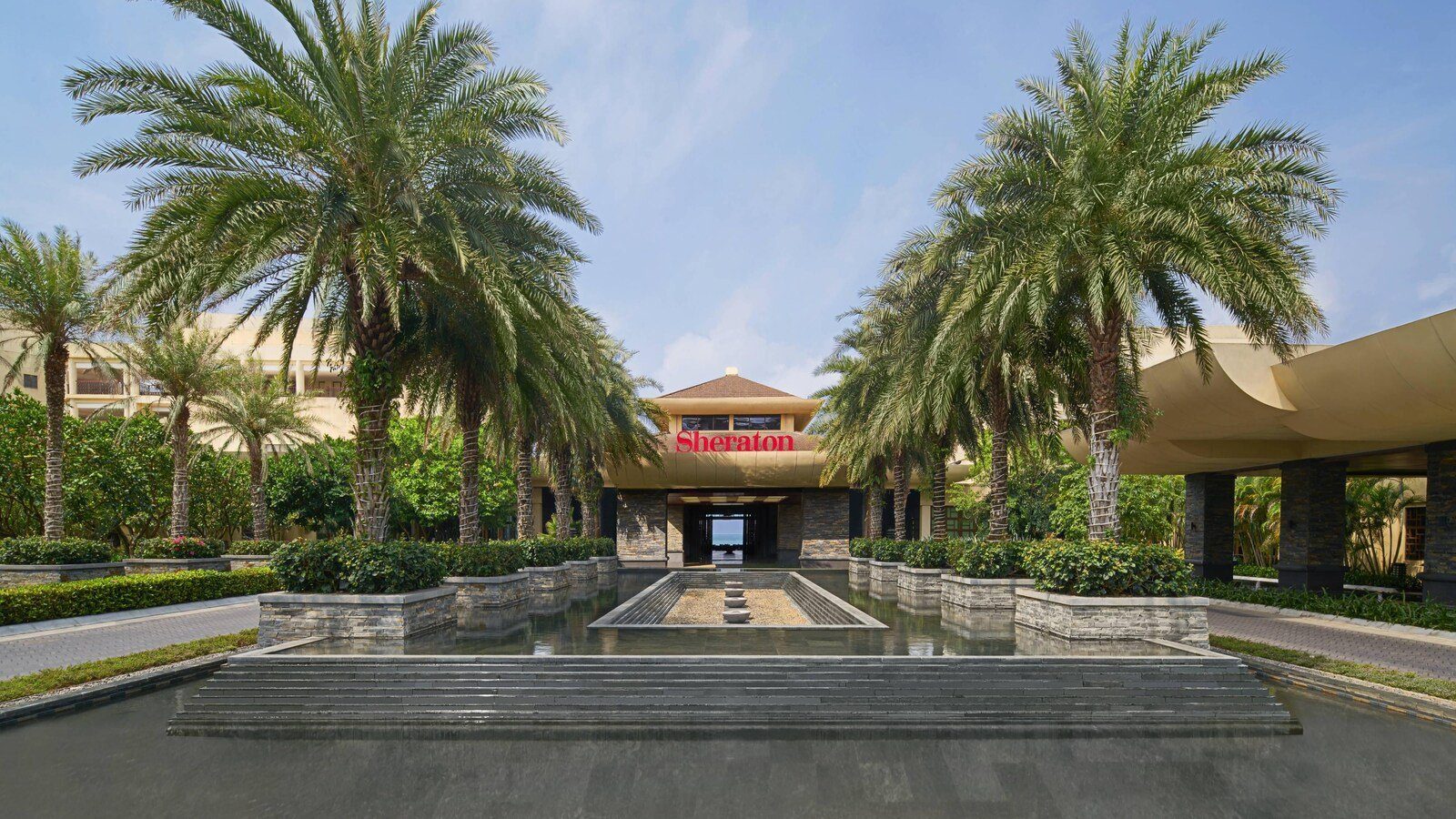 入口前的長方形水景兩側種著高大棕櫚樹，盡頭是掛著 Sheraton 字樣的大門