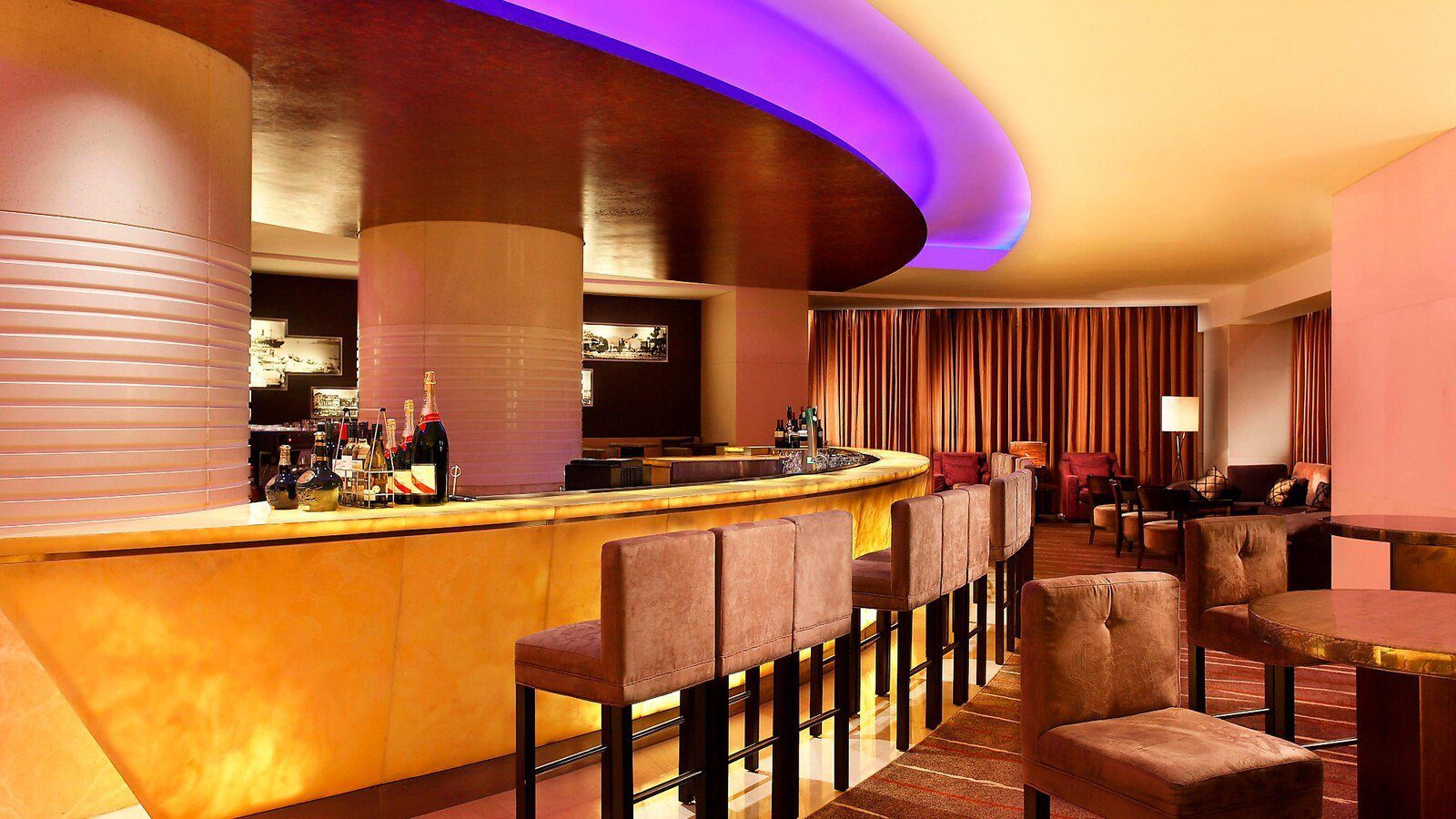 廈門喜來登酒店 Vista Lounge：弧形吧檯下方透出暖黃燈光，前方排列絨布高腳椅，上方是紫色燈帶的弧形天花，右後方為沙發座區