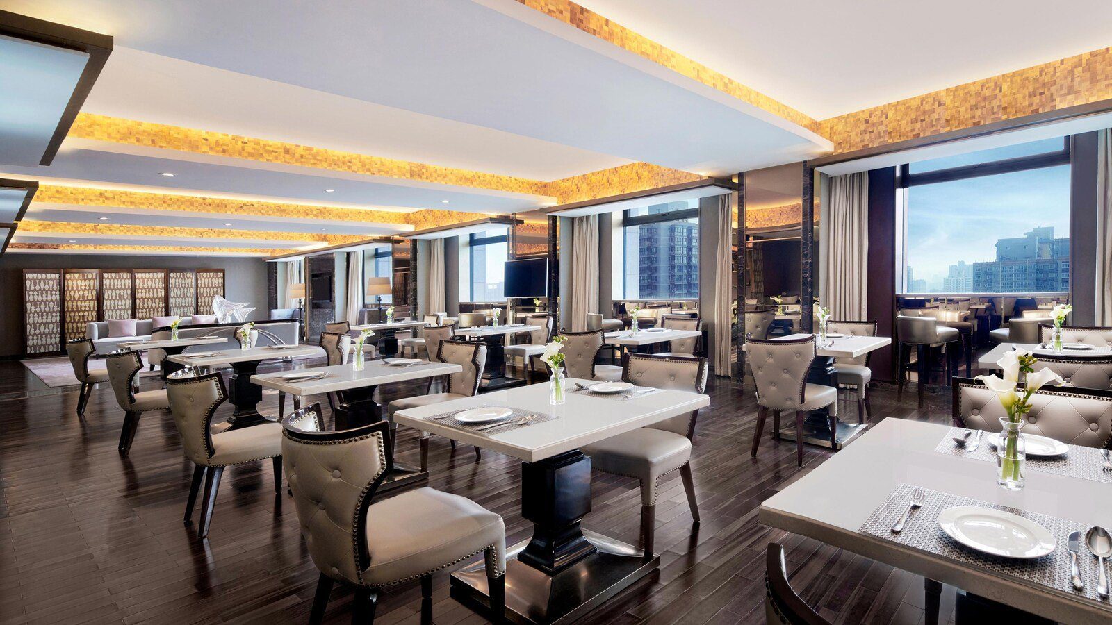 西安賽瑞喜來登大酒店 Sheraton Club 行政酒廊，深色木地板上排著白色桌面餐桌與灰色皮椅，天花有暖黃燈帶，右側大窗外是市區高樓