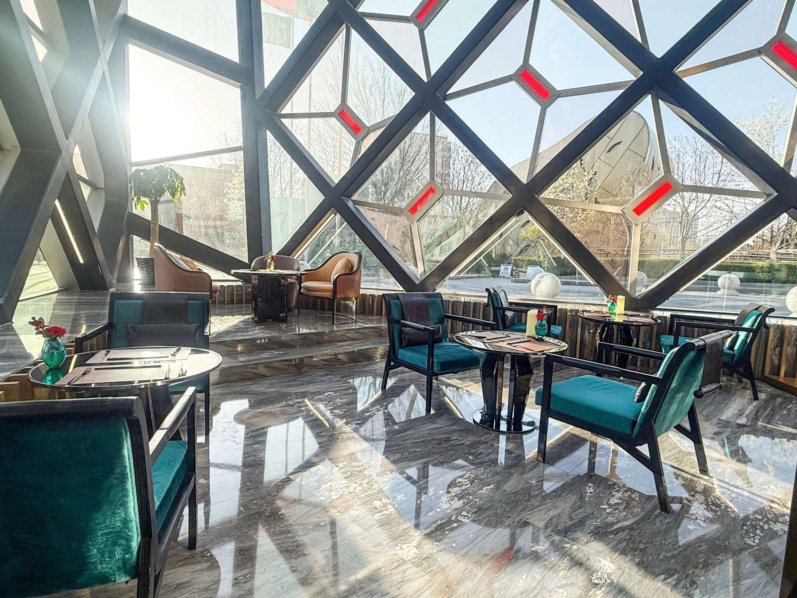 北京索菲特大酒店樂廊，菱格鋼構玻璃窗灑進陽光，墨綠絨布扶手椅圍著深色圓桌，窗外是綠樹與戶外廣場