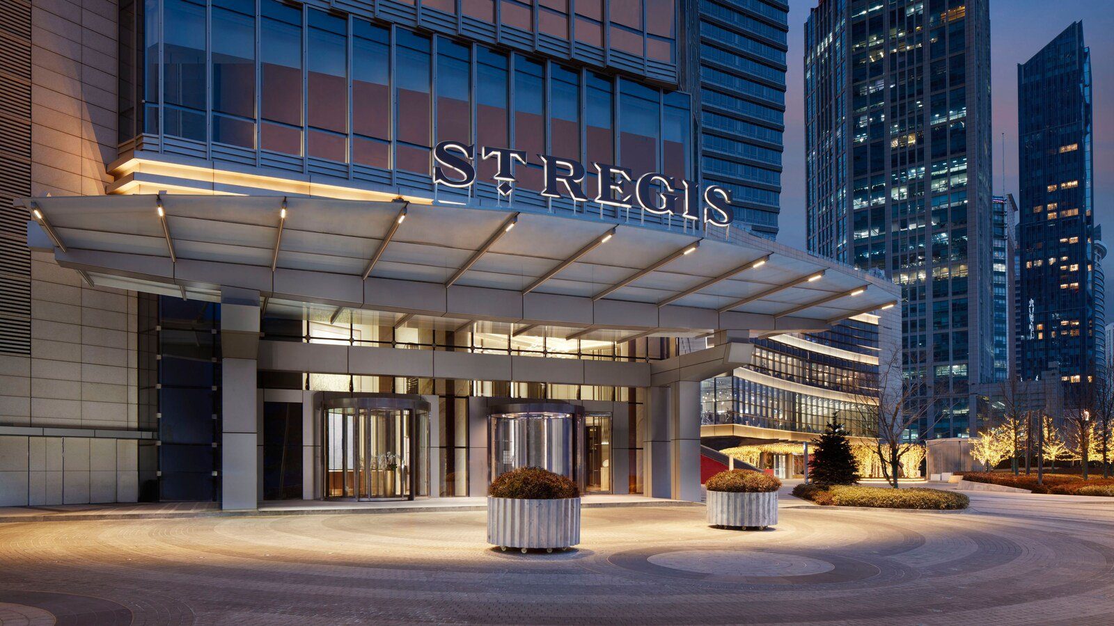 青島瑞吉酒店夜間入口，雨遮上方掛著 ST REGIS 字樣，前方是鋪著圓形石紋的車道