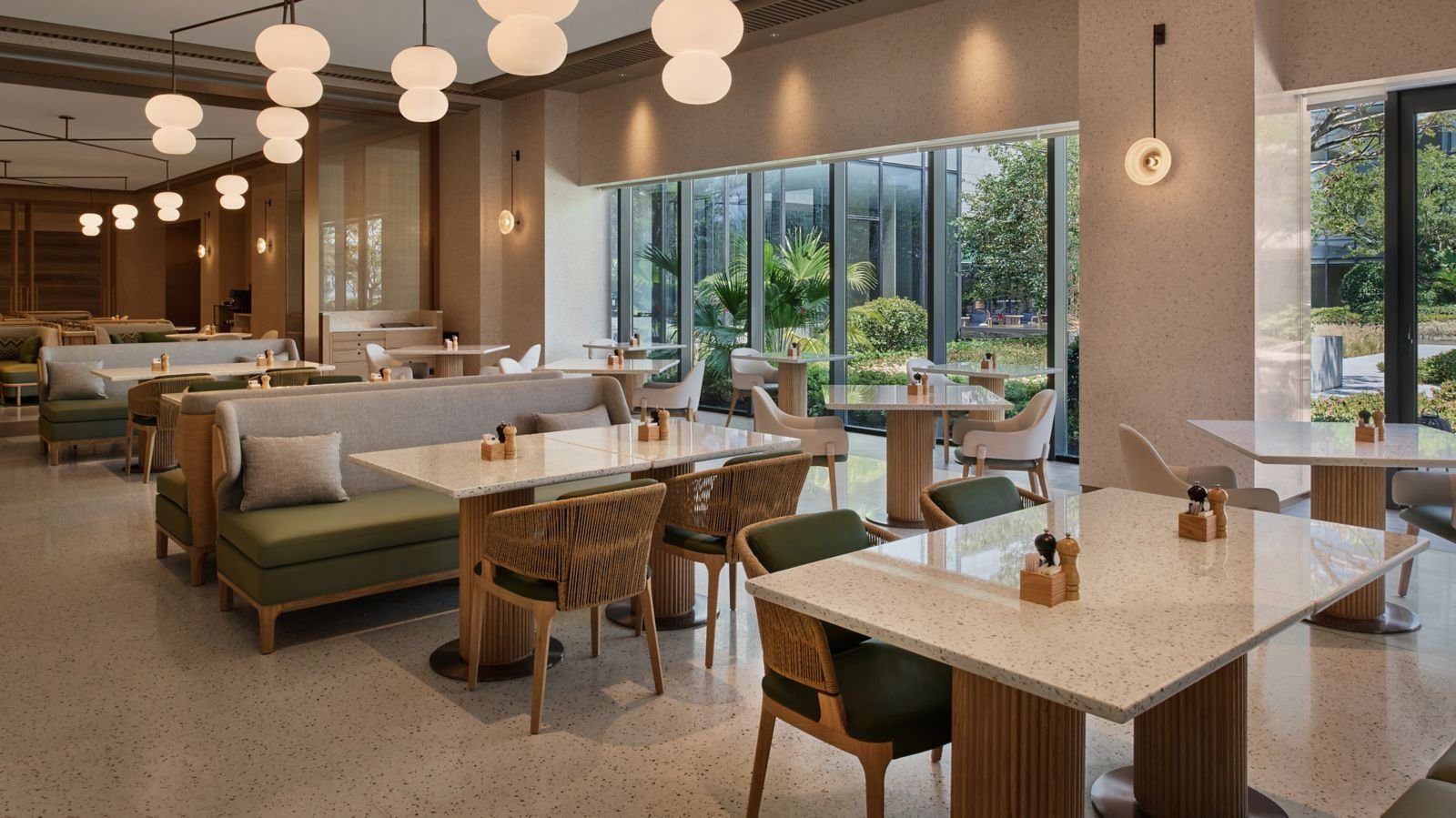 蘇州陽澄湖泰康萬豪酒店館內餐廳的用餐區：白色球形吊燈成列、水磨石方桌配藤編與綠色餐椅，落地窗外是棕櫚與庭院綠意