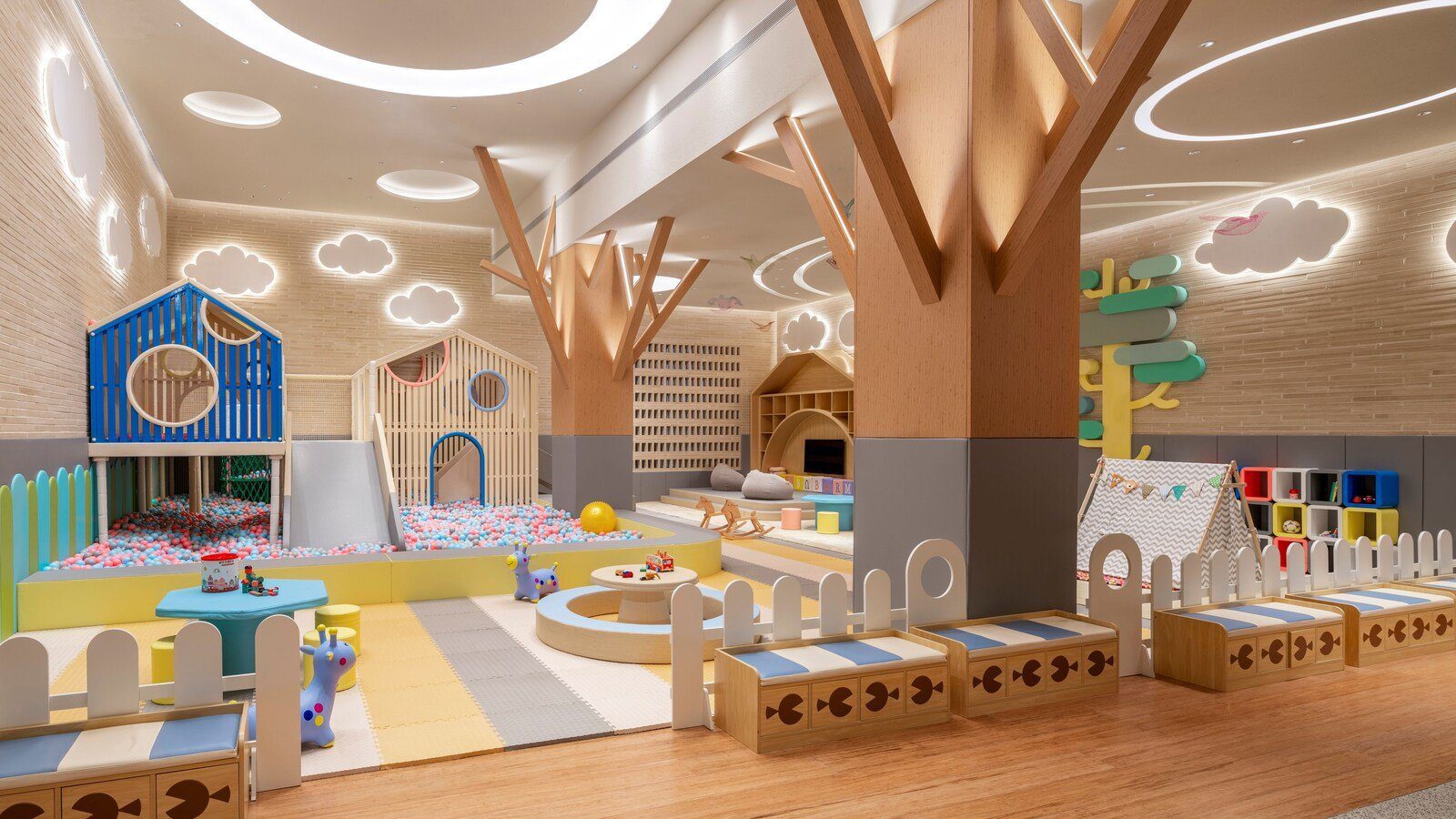 室內兒童樂園裡有藍色小屋造型的溜滑梯與球池，樹幹造型柱子撐起雲朵燈飾天花，旁邊是帳篷與積木櫃