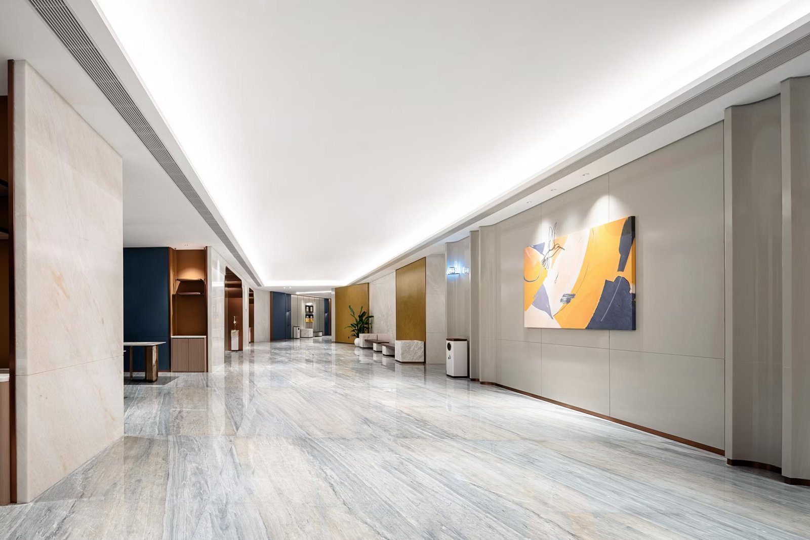 成都春熙路 voco 酒店館內長廊:淺灰色大理石地坪延伸到深處,右側牆面掛黃藍色抽象畫,左側是藍色牆面與木質展示櫃