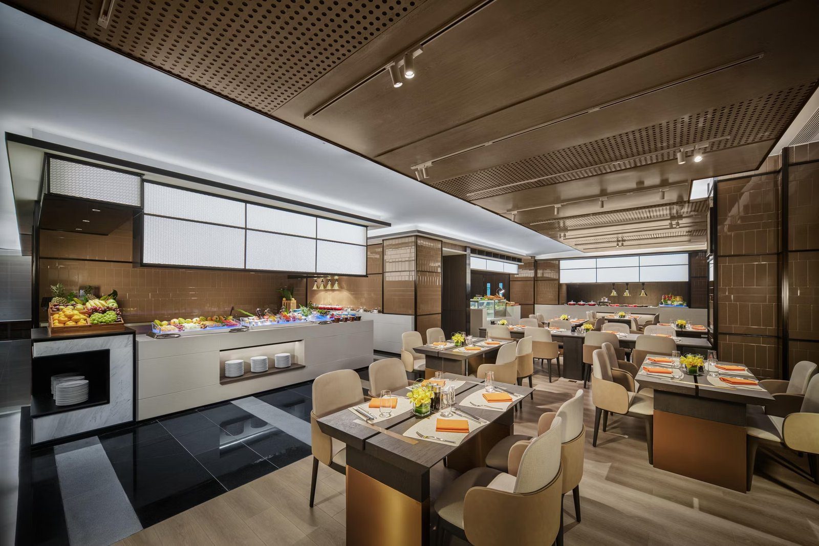 成都九眼橋 voco 酒店品味·匯花園餐廳:左側長形自助餐檯擺著水果與冰檯,右側是四人桌與米色皮椅,天花為穿孔木板與軌道燈