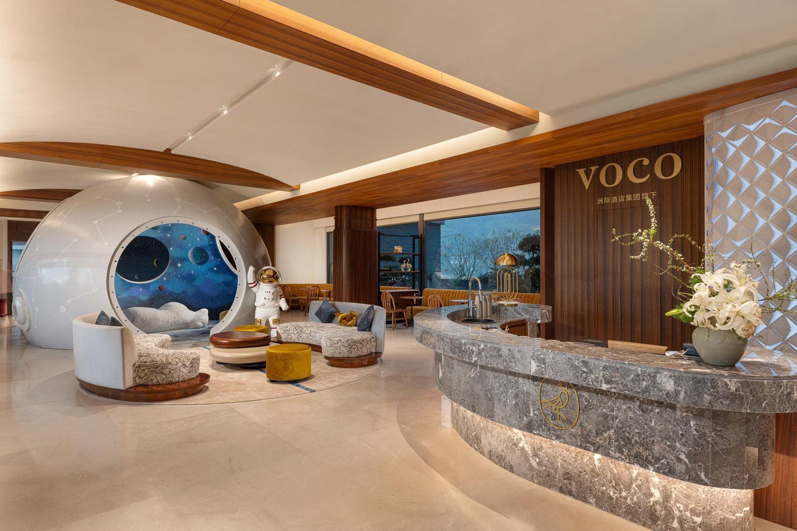 桂林陽朔 voco 酒店的大堂，右側是灰色大理石弧形接待櫃台與 VOCO 字樣木牆，左側是白色太空艙造型的休息區與太空人擺飾