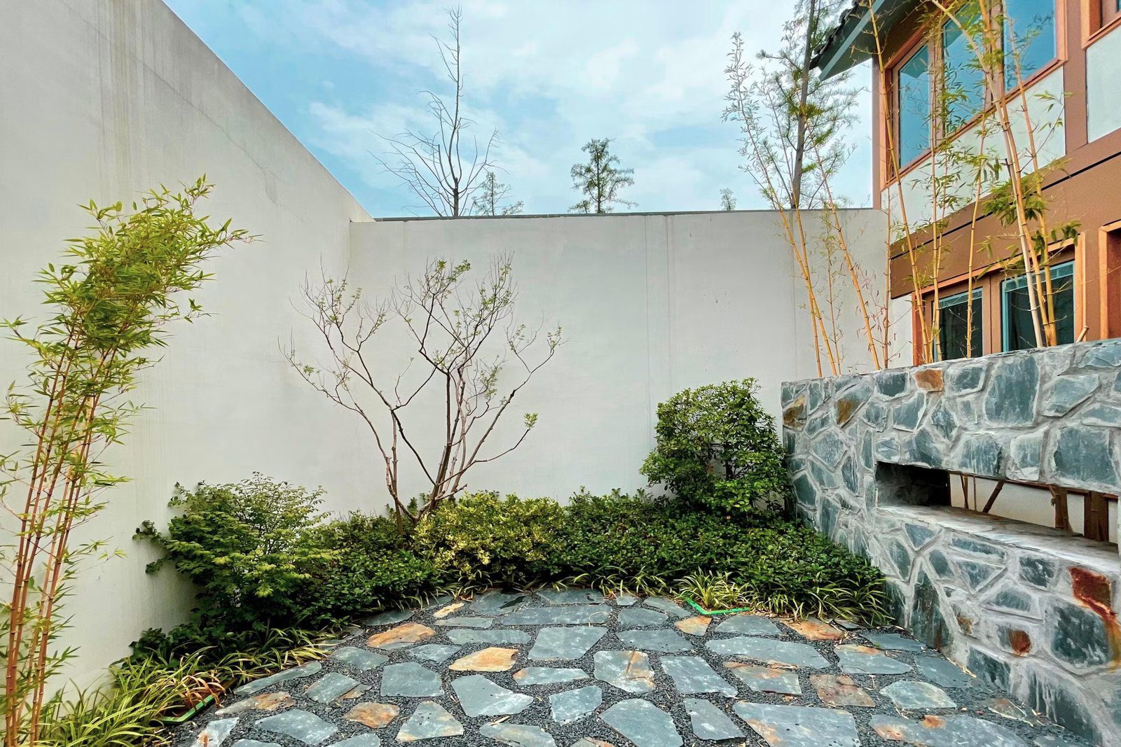 南京園博園voco酒店客房的私人庭院，白牆圍起的石板地上種著竹子與灌木