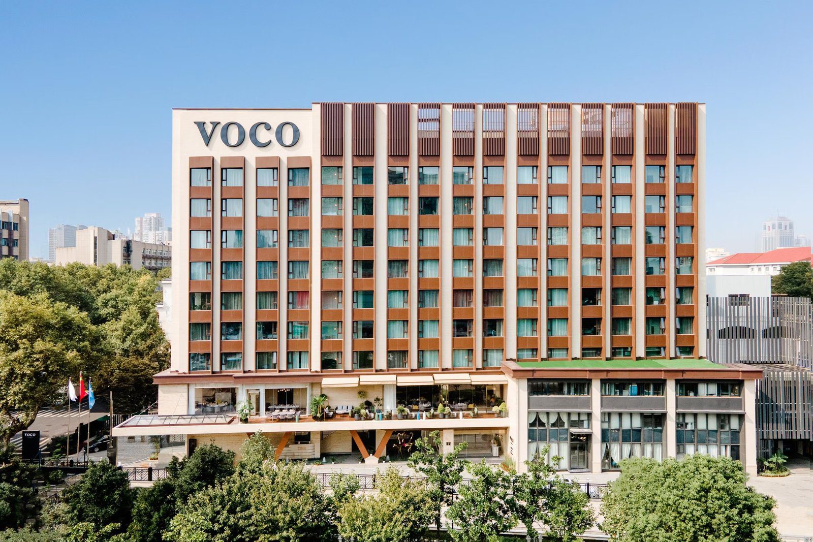 南京東方珍珠voco酒店白天外觀，磚紅色與米白色相間的立面，2 樓外側是擺著桌椅與盆栽的露台