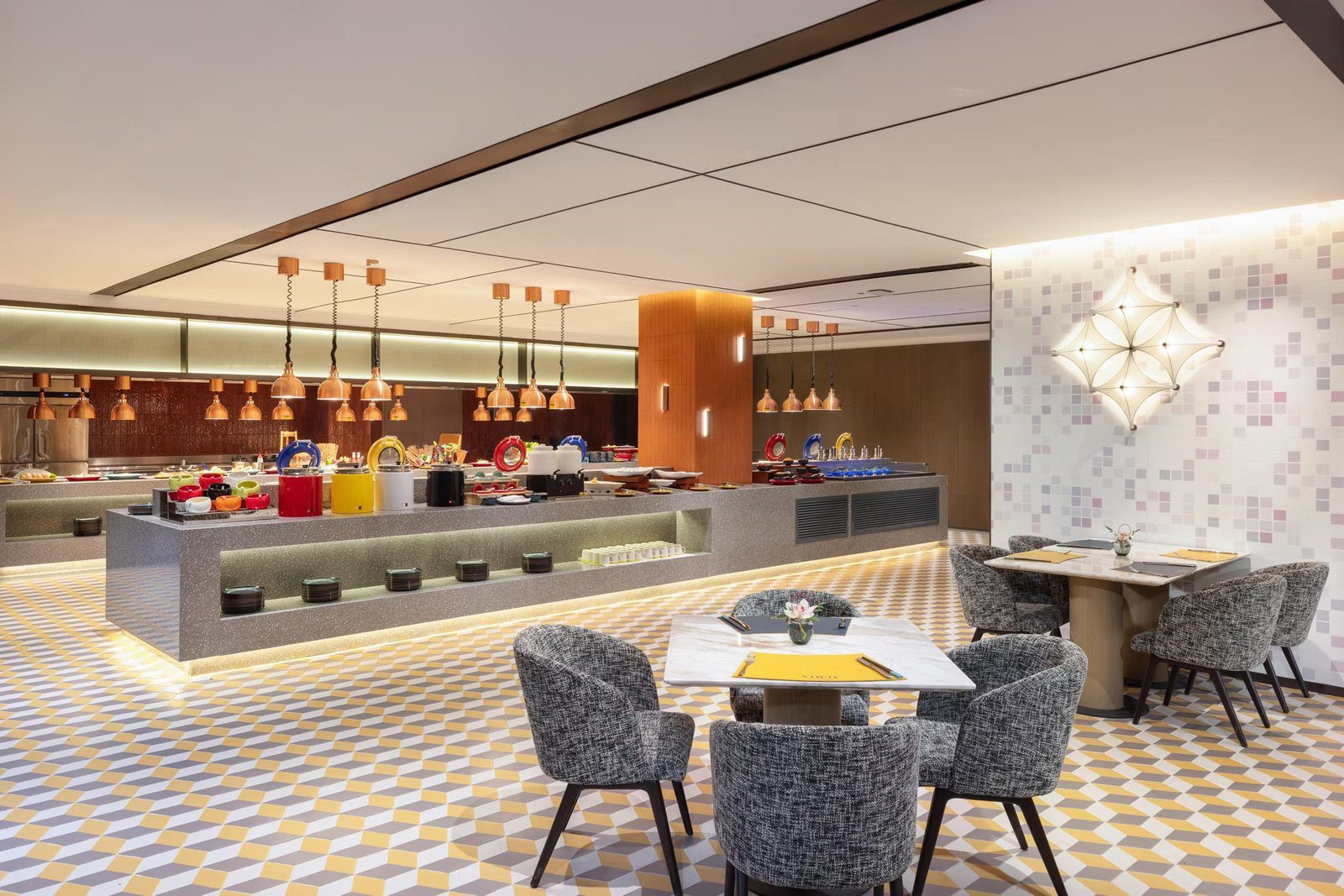 蘇州觀前街 voco 酒店 V Kitchen 全日餐廳的長形自助檯與成排銅色保溫吊燈，前方是黃白幾何地坪與灰色扶手椅餐桌