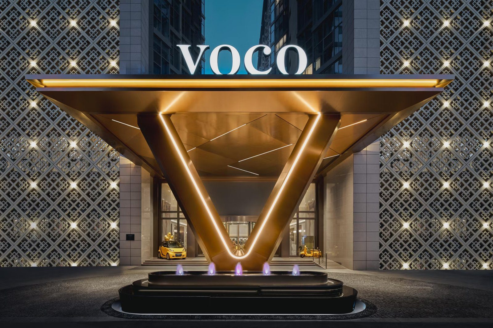 入夜的西安秦都傳奇 voco 酒店主入口,V 字形金色雨遮柱上方是 VOCO 招牌,前方有噴泉水池,兩側是鏤空花格立面