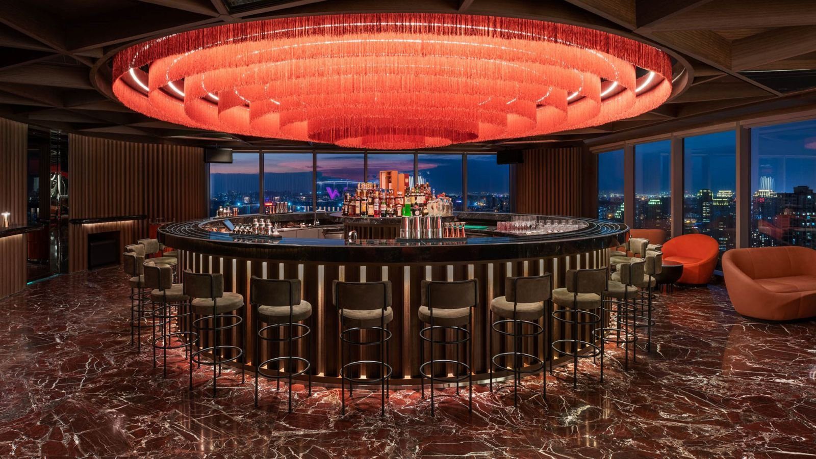 廈門 W 酒店 HEAT 酒吧：圓形吧檯上方是紅色流蘇圓形燈飾，周圍排列高腳椅，地面為深紅色大理石，落地窗外是城市夜景