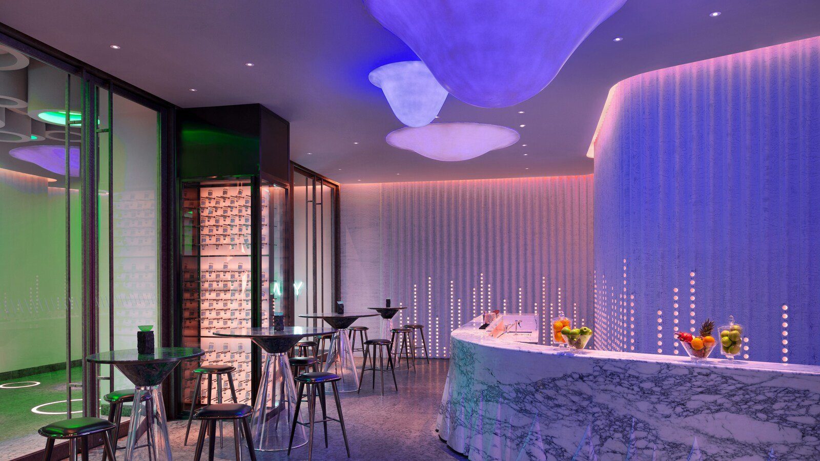 西安 W 酒店 AWAY 水療的休息吧，白色大理石弧形吧台上擺著水果，後方是點點燈光的直紋弧牆，天花垂著雲朵狀的藍紫色燈飾，左側是高腳桌椅