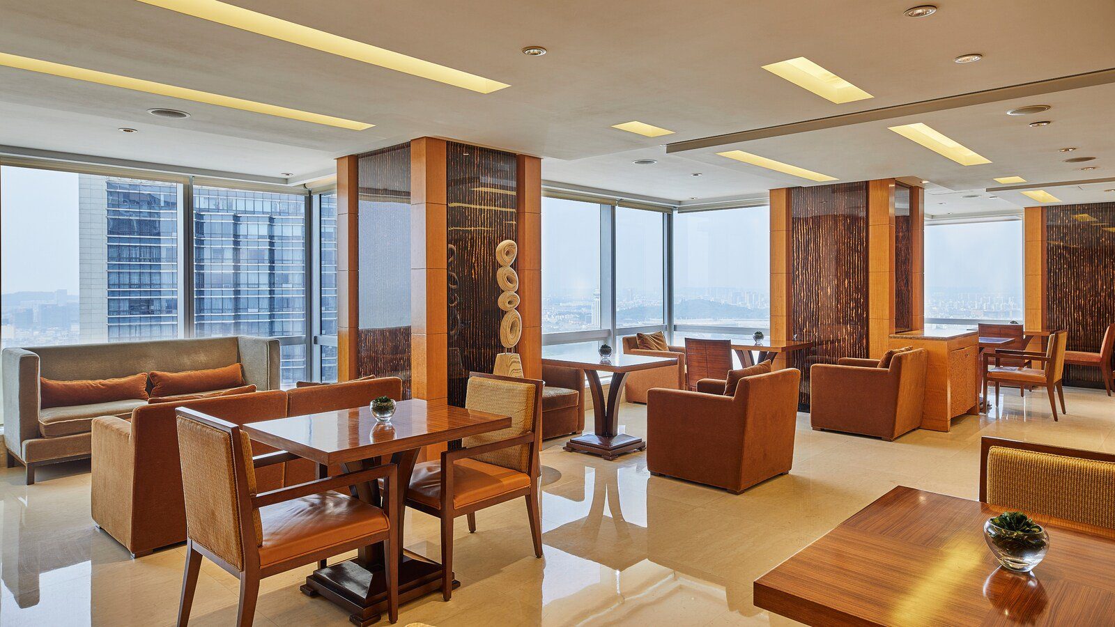 南京金茂威斯汀大酒店的 Westin Club 酒廊，落地窗邊擺著橘色絨布沙發與木桌，窗外是市區與遠山