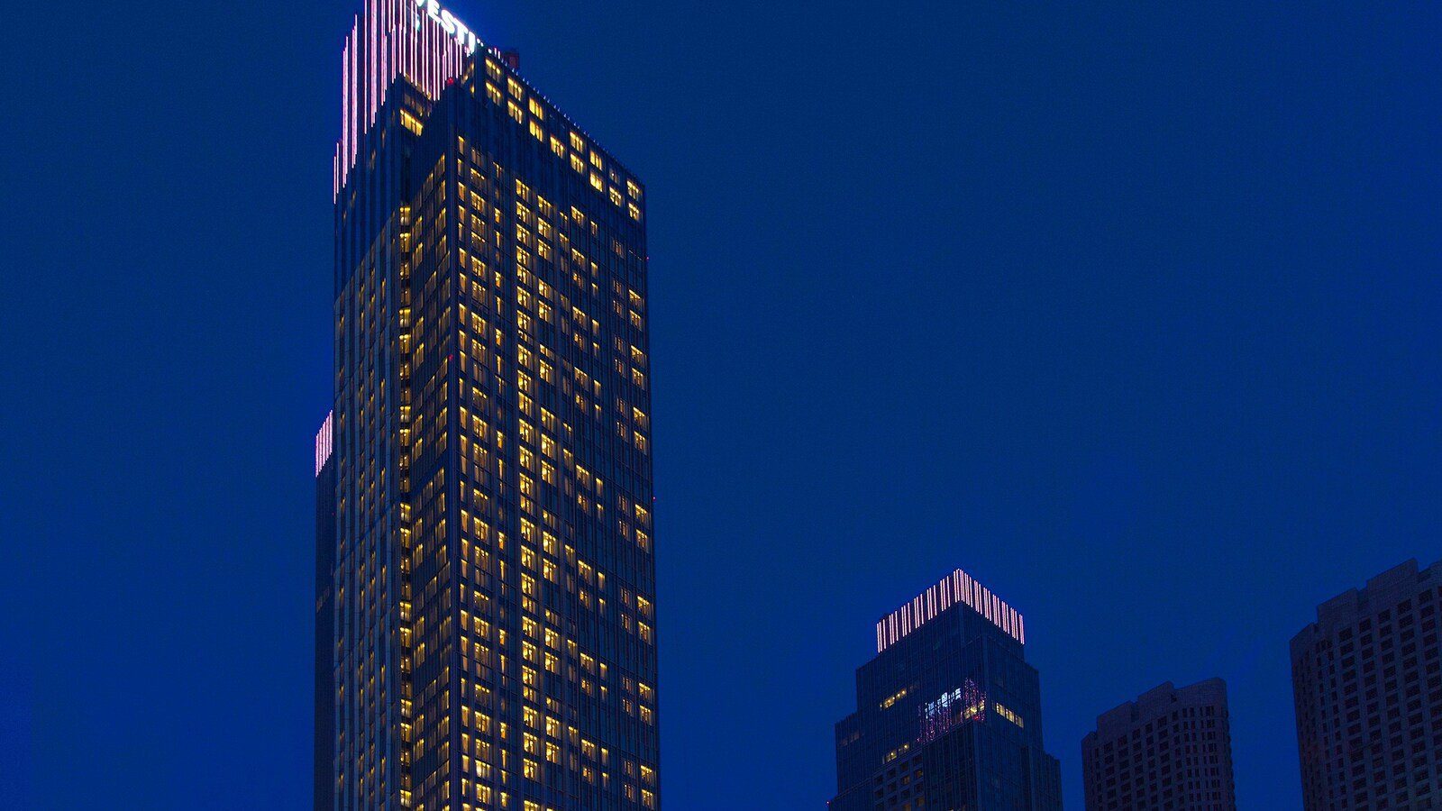 青島威斯汀酒店塔樓夜景，整棟大樓窗戶亮著燈，頂端亮著館名字樣