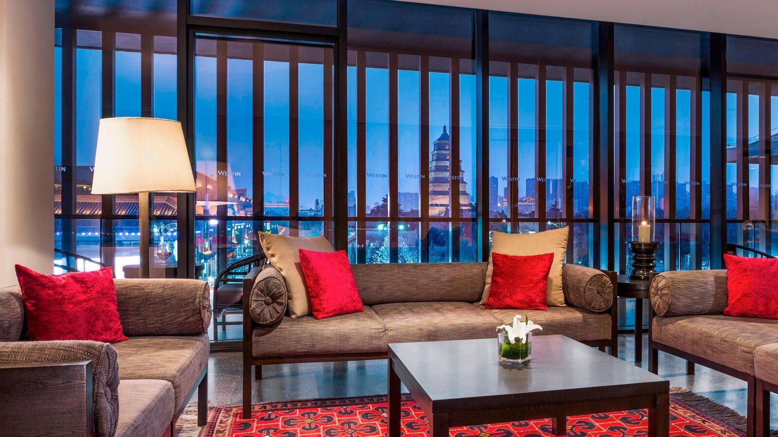 西安威斯汀大酒店 Westin Club 行政酒廊，紅色抱枕的布沙發圍著深色方几，整面落地窗外是藍色夜空下亮燈的大雁塔與城市