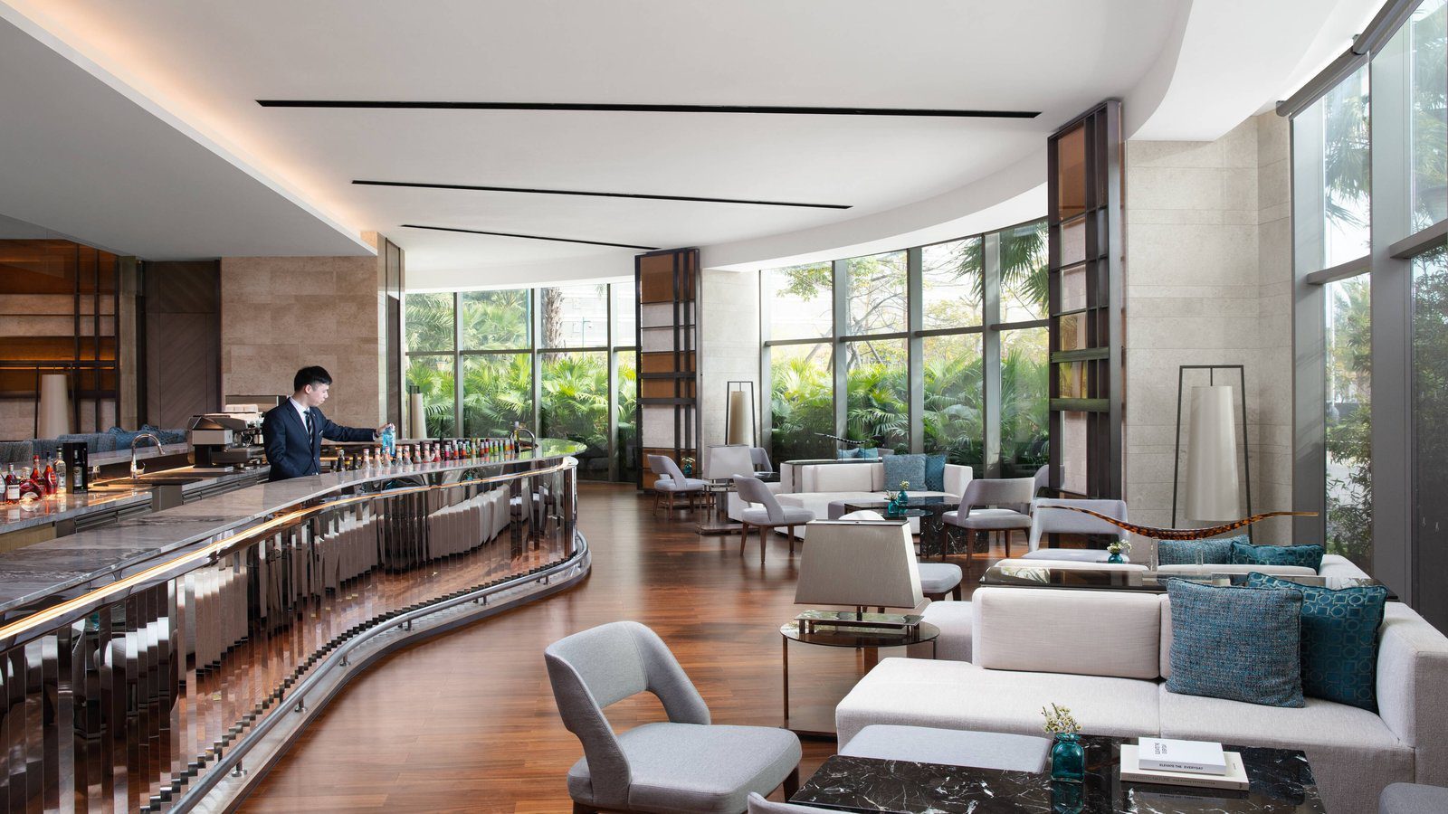 廈門泰地萬豪酒店 The Lounge，左側是弧形長吧檯，右側白色沙發與扶手椅臨著整面落地窗，窗外是綠植