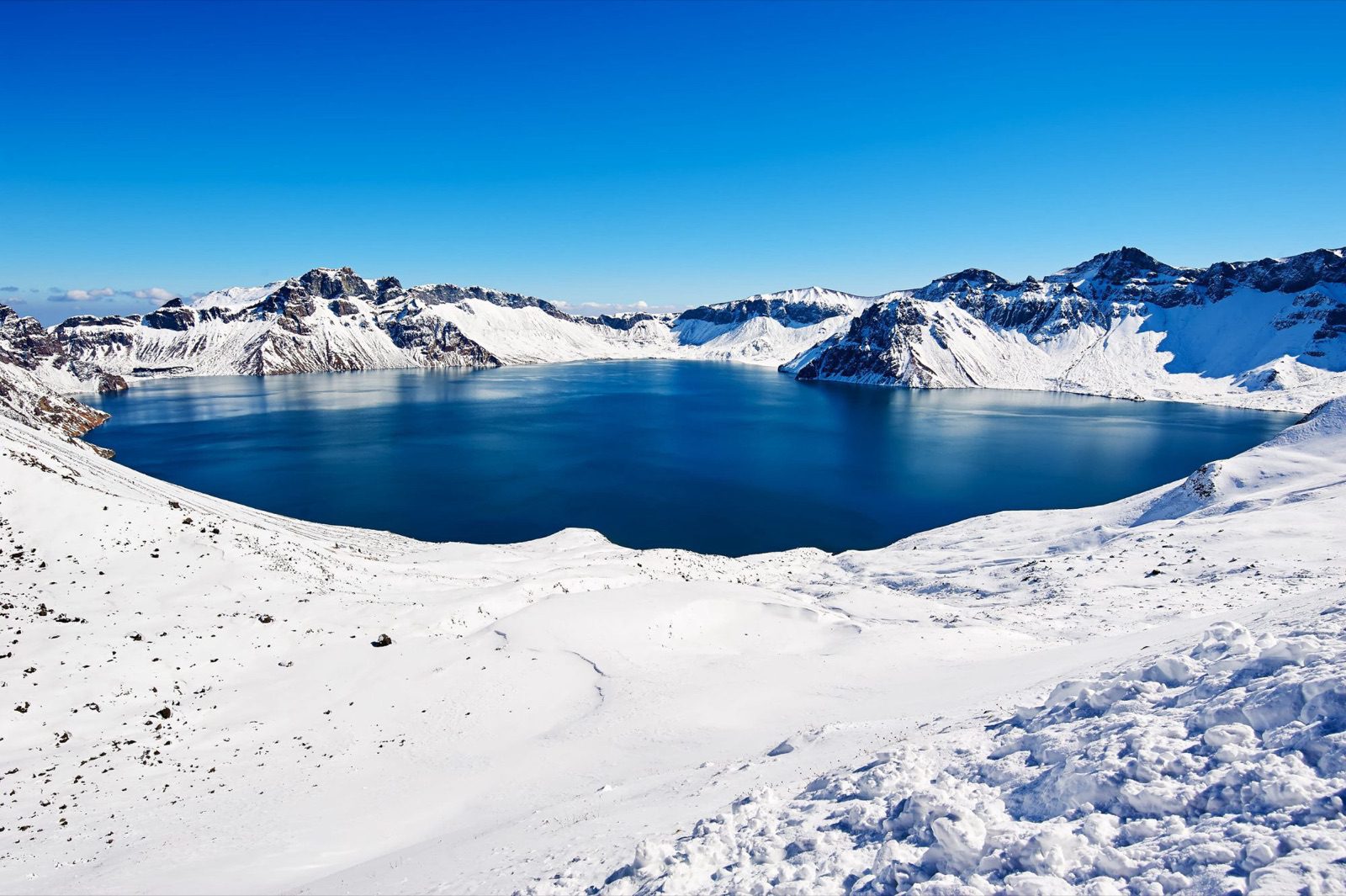長白山天池雪季晴空,深藍湖面被積雪火山口環繞