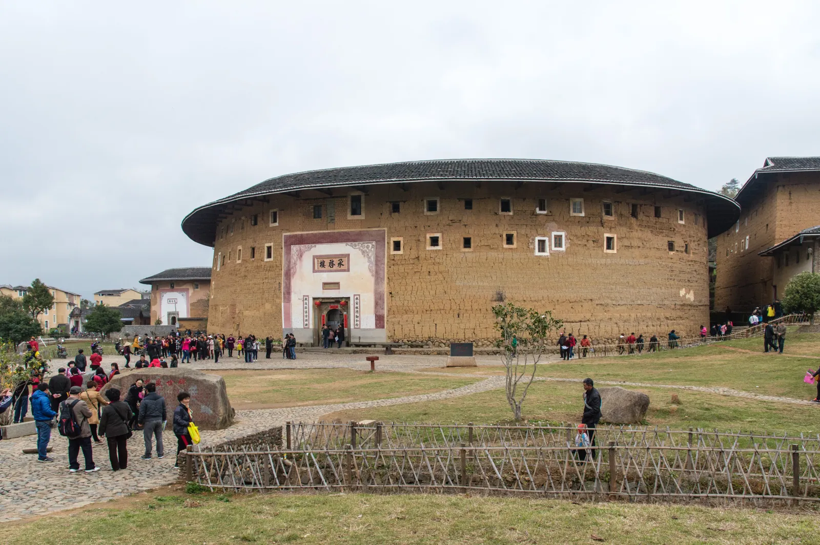 夯土外牆的圓形土樓與門前草地上的參觀旅客