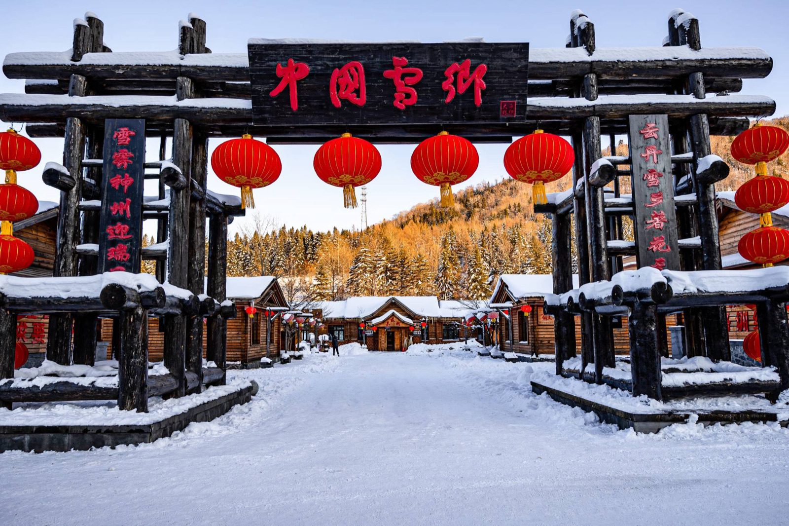 雪鄉入口木造牌樓掛滿紅燈籠,後方是積雪木屋